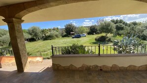 A covered patio with a view of a grassy area and parked cars.