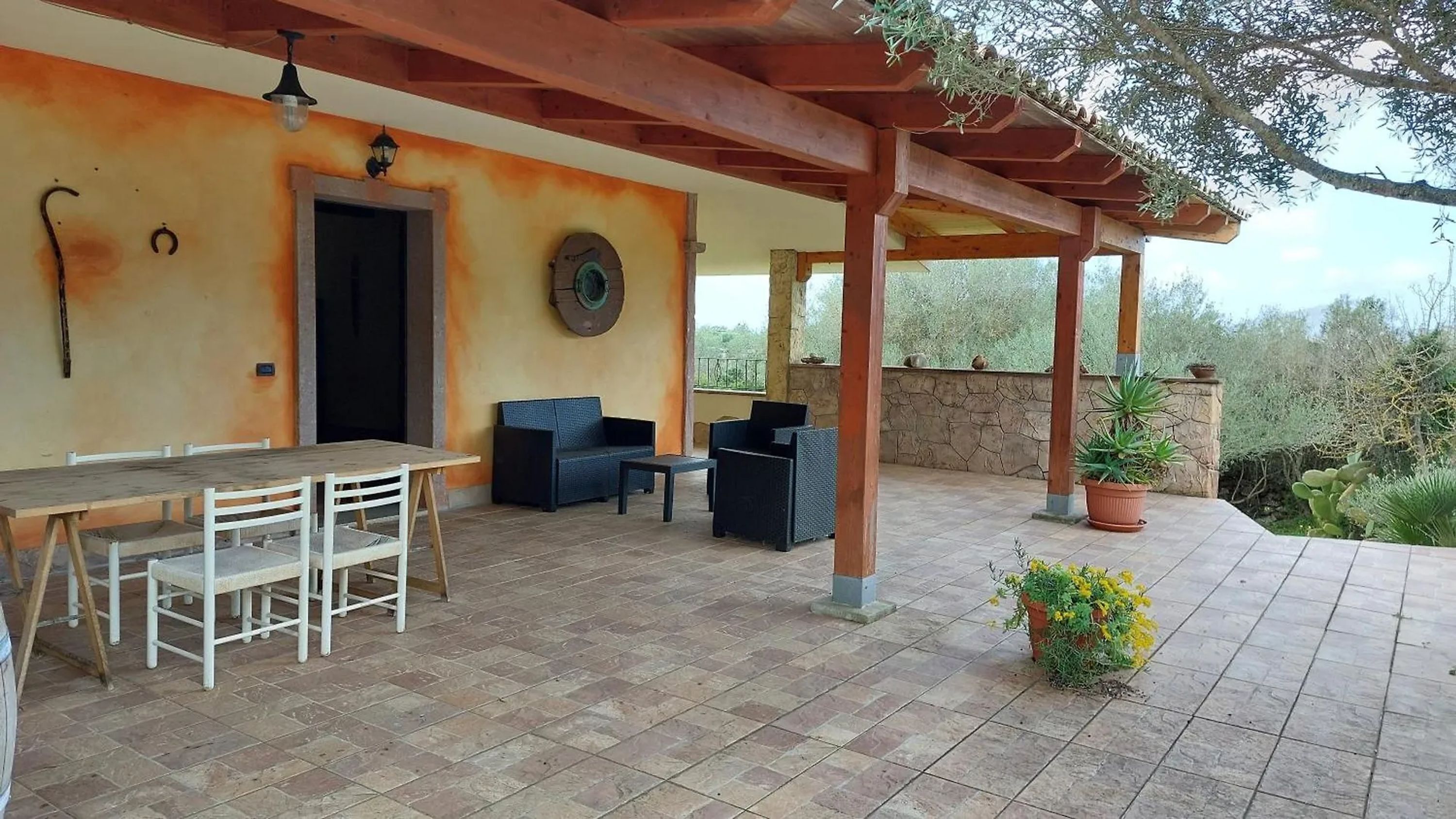 A covered patio area with a table and chairs, a stone wall, and potted plants.