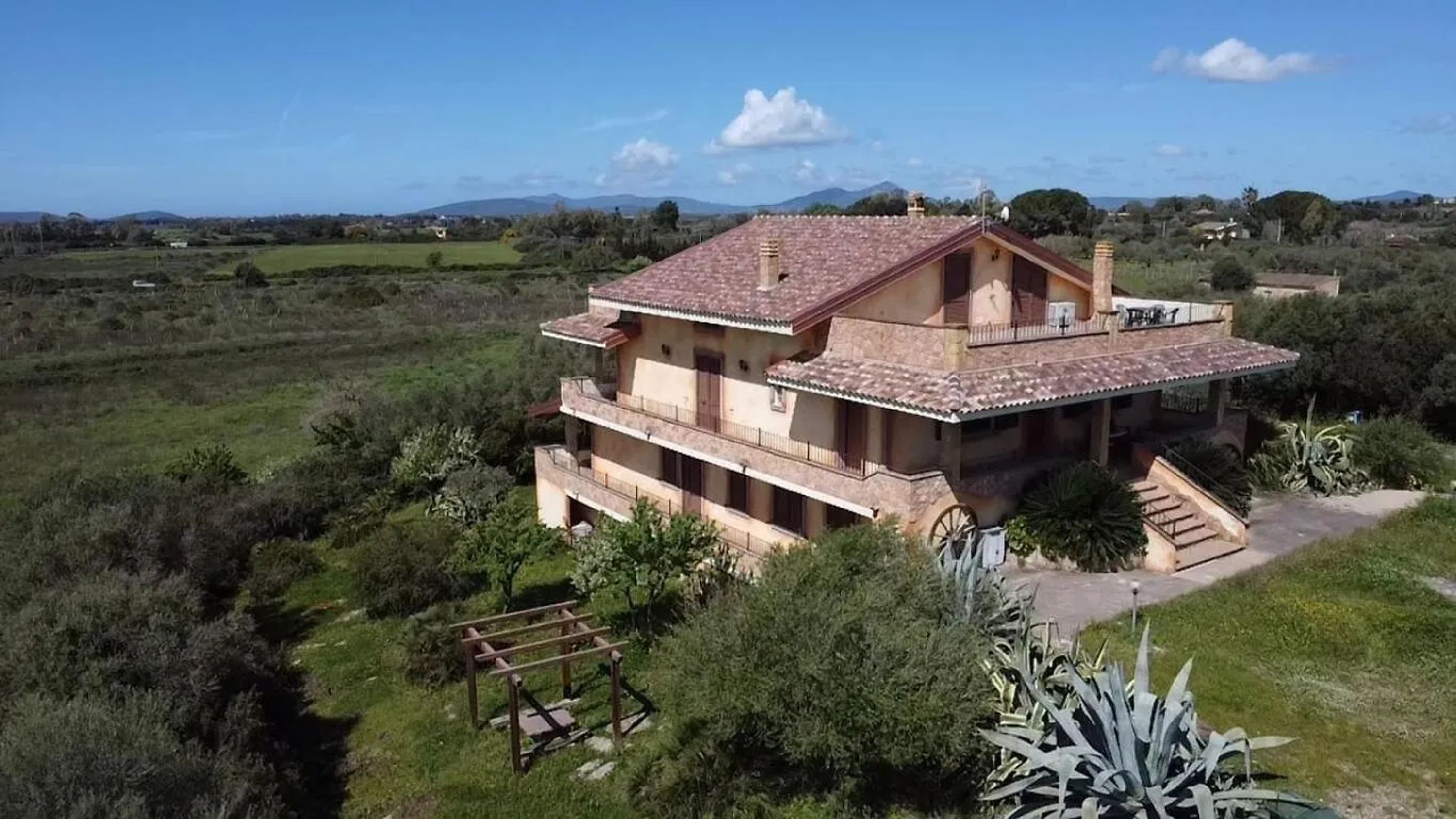 A two-story house with a tiled roof, surrounded by greenery and a clear sky.