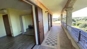 Un balcon doté d’un sol à carreaux, de portes en bois et offrant une vue sur la verdure.