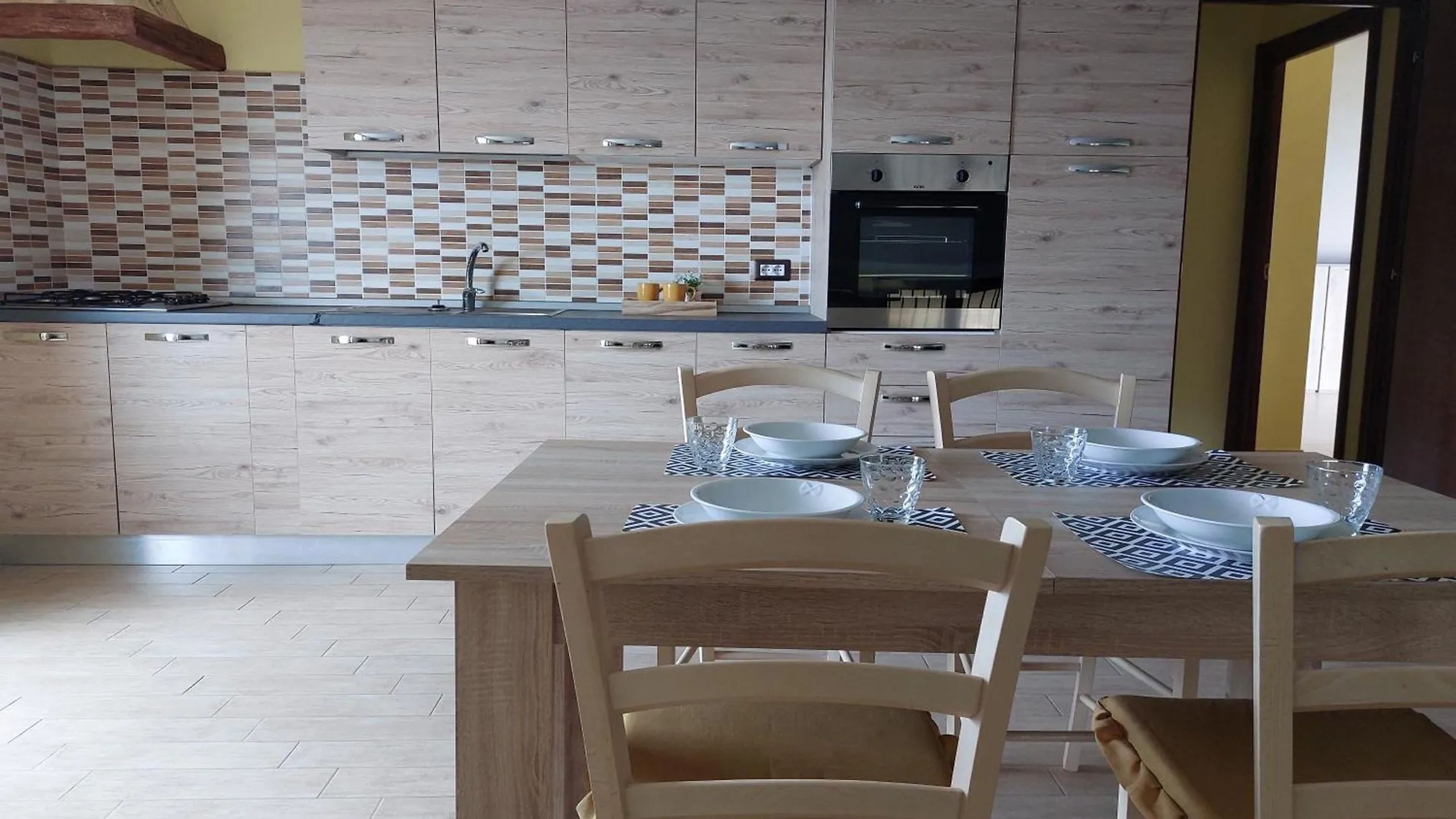 A modern kitchen with a tiled backsplash, a built-in oven, and a dining area with a table set for four.