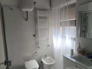 A bathroom with a toilet, bidet, sink, and a shower area.