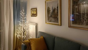 Olohuoneessa on sohva, patteri ja kaksi kehystettyä kuvaa seinällä.