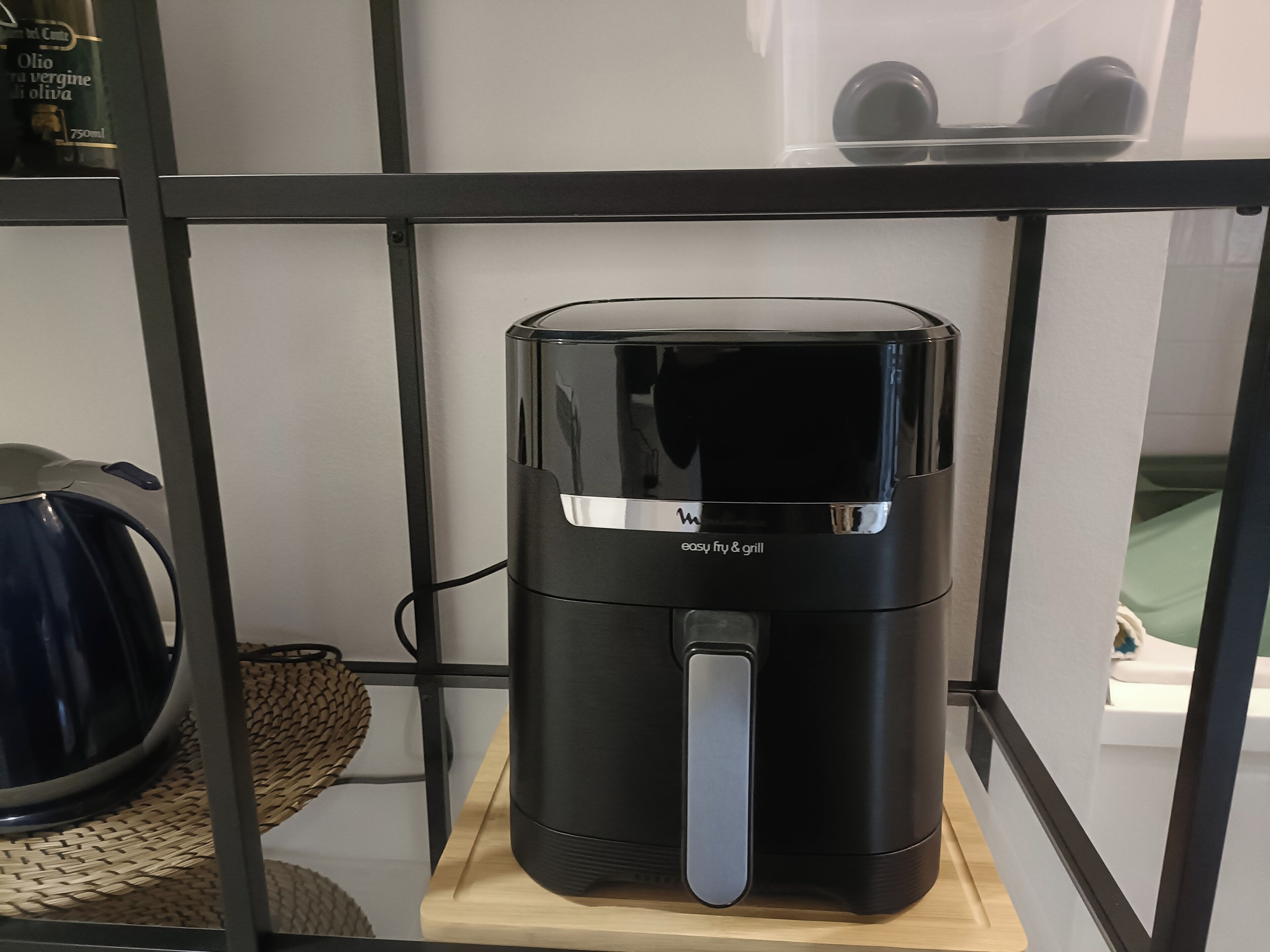 A black coffee maker on a wooden shelf in a room with a metal frame shelf and a woven basket.