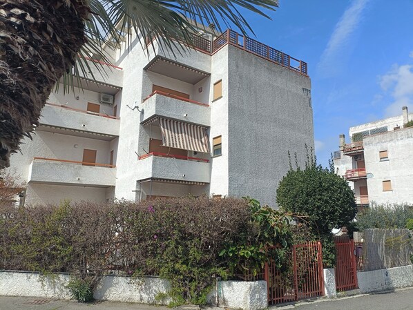 A multi-story residential building with balconies, a gated entrance, and surrounding vegetation.