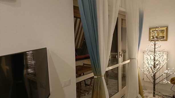 Huoneessa on televisio, ikkunassa verhot, patteri ja koristeellinen valaistu puu.
