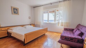 Un dormitorio con una cama de madera, un sofá morado, una ventana con cortinas y un cuadro en la pared.