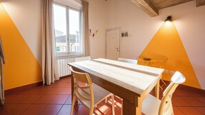 A dining area with a wooden table and chairs, a window with curtains, and a ceiling with exposed beams. - Yellow Home by MMega (Florence)