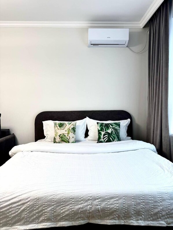 Une chambre d’hôtel avec un lit, du linge de lit blanc, une tête de lit sombre et un appareil de climatisation fixé au mur.