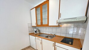 A compact kitchen with white cabinets, a wooden countertop, a built-in oven, and a sink. - Apartman Villa Ljiljana 2 (Jadranovo)