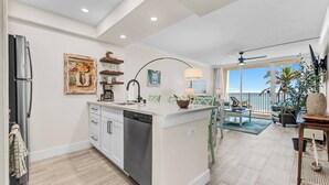 Una cocina moderna con lavavajillas, un comedor con vista al océano y un balcón con plantas.
