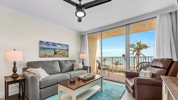 Una sala de estar con un sofá gris, un sillón de cuero marrón, una mesita de centro y un cuadro de una escena de playa.