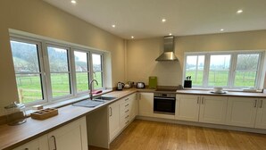 Una cocina amplia con ventanas grandes, piso de madera y muebles de cocina blancos.