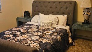 Ein ordentlich bezogenes Bett mit Blumenmuster, einem gepolsterten Kopfteil und einer Nachttischlampe auf einem Beistelltisch.