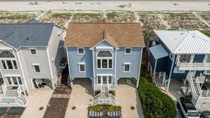 Una propiedad frente a la playa con una casa de dos pisos, un porche delantero y un patio cubierto.