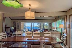 A dining area with a wooden table and chairs, a television, and a view of the sea.