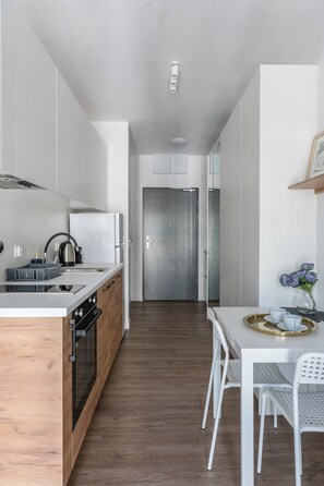 A modern kitchen with white cabinetry, a wooden countertop, and a stainless steel refrigerator. There is a dining area with a white table and chairs, and a vase with flowers on the wall.