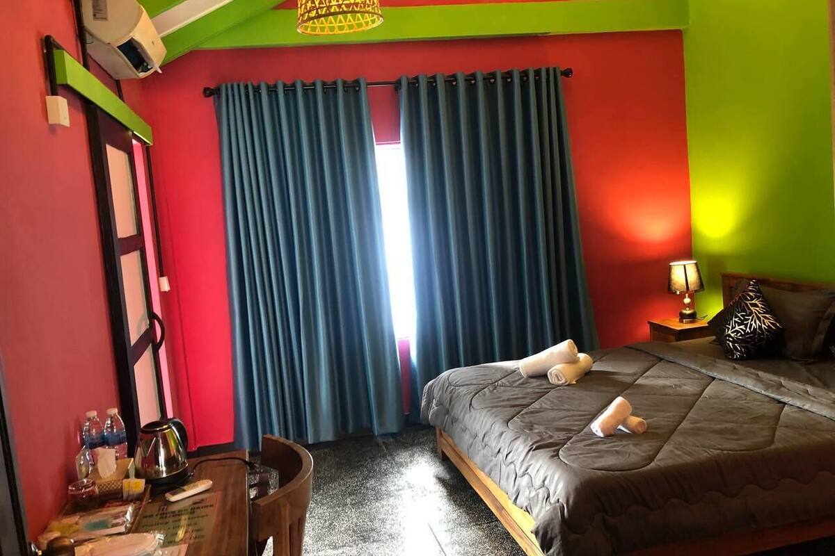 A hotel room with a bed, a desk, a chair, a lamp, and a window with curtains.