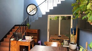 A home office with a desk, laptop, and computer monitor. There is a staircase with a railing, a dining table with chairs, and a potted plant. - Bat Chum Villa (Phnom Penh)