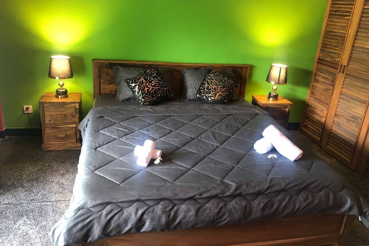 A bed with a dark quilted cover, two bedside lamps, and patterned pillows.