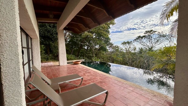 Un espacio al aire libre cubierto con piscina, sillones de descanso y vistas a la vegetación circundante.