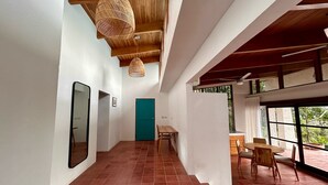 Un pasillo espacioso con techo de madera, una puerta verde y un comedor con mesa y sillas.