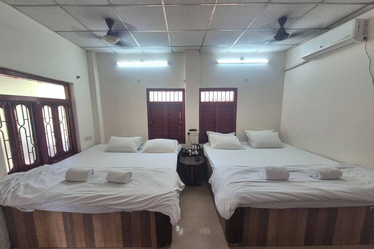 A room with two beds, each with white linens and pillows, a small table with a lamp, and a ceiling fan.