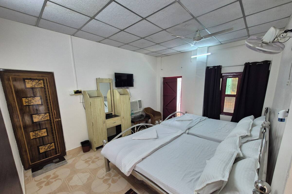 A hotel room with a large bed, a wooden wardrobe, a desk with a chair, a television, and a window with curtains.