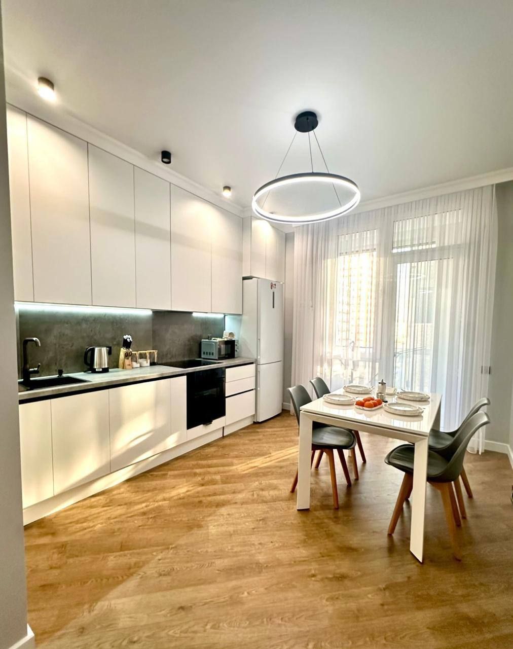 Eine moderne Küche mit weißen Schränken, einer schwarzen Arbeitsplatte und einem Essbereich mit Tisch und Stühlen.
