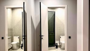 Un couloir au plancher de bois menant à une salle de bain équipée de toilettes, d’un bidet et d’une douche.