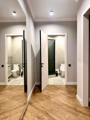 A hallway with a wooden floor leading to a bathroom with a toilet, bidet, and shower.