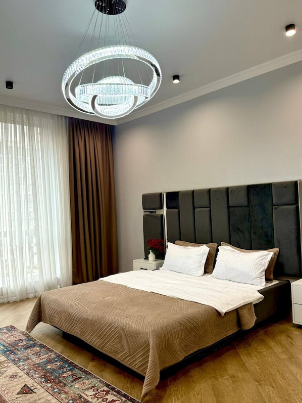A modern bedroom with a large bed, a decorative ceiling light, a nightstand, and a patterned rug.