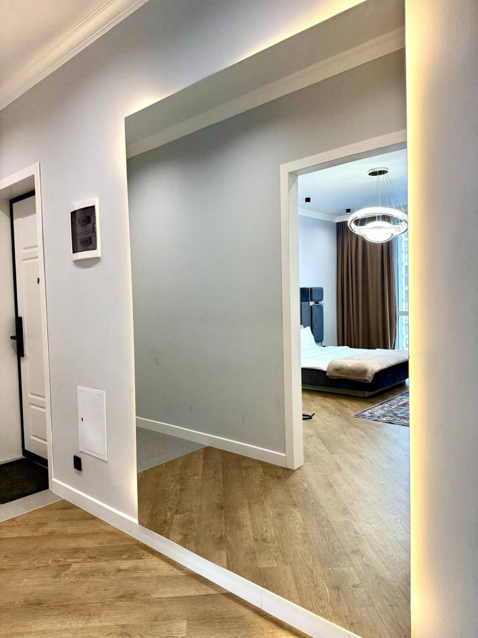 Ein modernes Hotelzimmer mit Holzboden, einem Bett mit Kopfteil und einem großen Fenster mit Vorhängen.