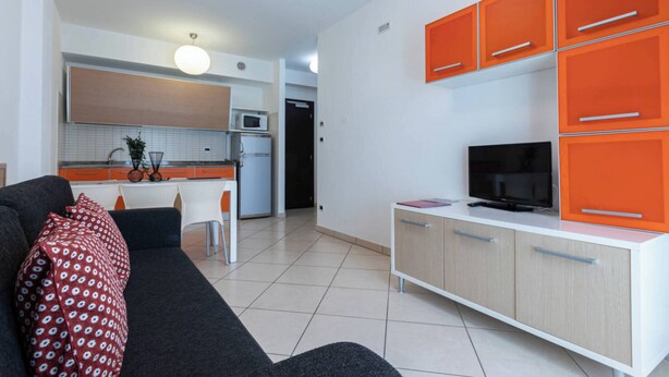 A modern living room with a sofa, a television, and orange cabinets.