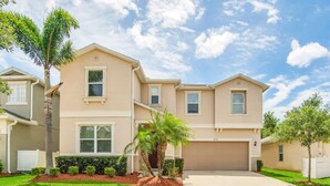 A two-story residential building with a beige exterior, a garage, and a well-maintained lawn with palm trees. - 4736 Family Home Near Disney Sea World (Kissimmee)