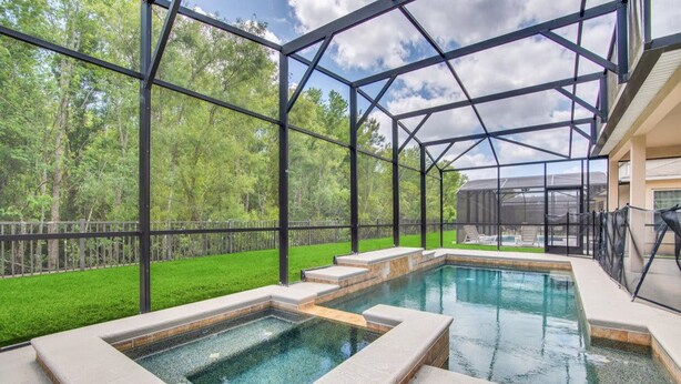 A glass-enclosed swimming pool area with a view of a green lawn and trees. - 4736 Family Home Near Disney Sea World (Kissimmee)