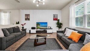A modern living room with two grey sofas, a glass coffee table, a flat-screen TV, and a decorative ceiling light. - 4736 Family Home Near Disney Sea World (Kissimmee)