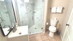 A bathroom with a glass shower enclosure, a white sink, and a toilet.