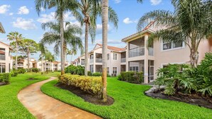 A residential complex with multiple two-story buildings, a paved pathway, and well-maintained greenery. - Right Direction Rentals 1 Bedroom Villa 9955 (Port St. Lucie)