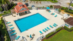 A swimming pool with sun loungers, a covered seating area, and a building with a red roof. - Right Direction Rentals 1 Bedroom Villa 9955 (Port St. Lucie)