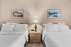 Een hotelkamer met twee bedden, een nachtkastje met een lamp en een klok, en twee ingelijste foto's aan de muur.