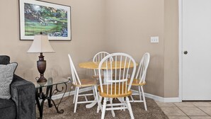 A room with a dining table, chairs, a lamp, a framed picture, a couch, and a door. - Right Direction Rentals 1 Bedroom Villa 9955 (Port St. Lucie)