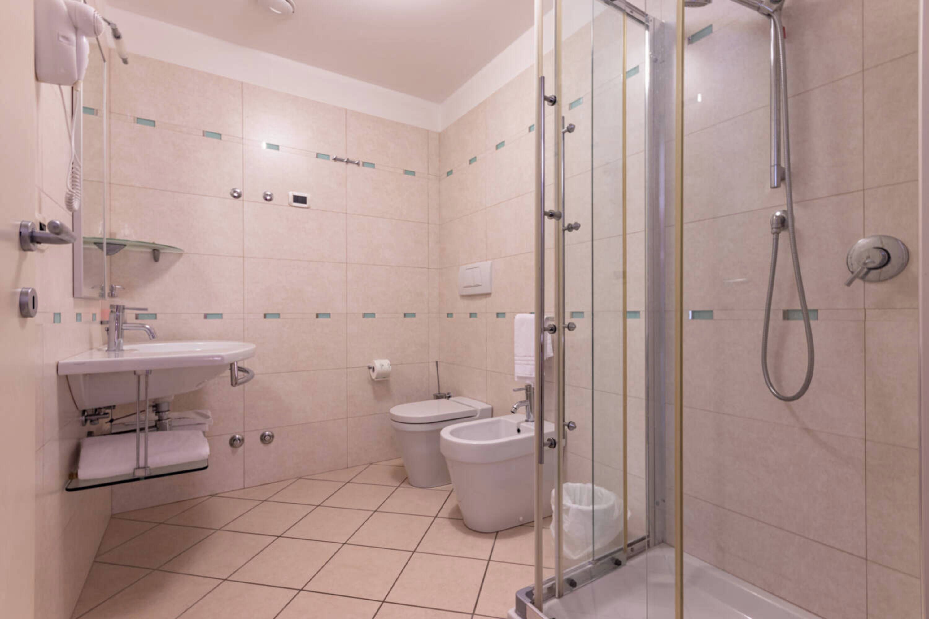 A modern bathroom with a glass-enclosed shower, a sink, a toilet, and a hairdryer mounted on the wall.