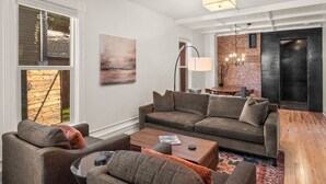 Una sala moderna con sofá, mesa de centro y comedor con pared de ladrillo y candelabro.