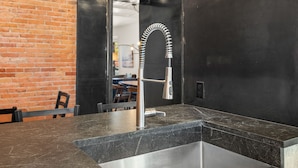 Una cocina moderna con encimera negra, pileta de acero inoxidable y pared de ladrillo a la vista.