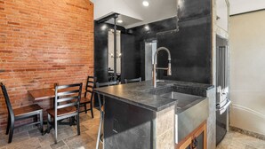 Una cocina con pared de ladrillo, encimera negra y pileta de acero inoxidable.