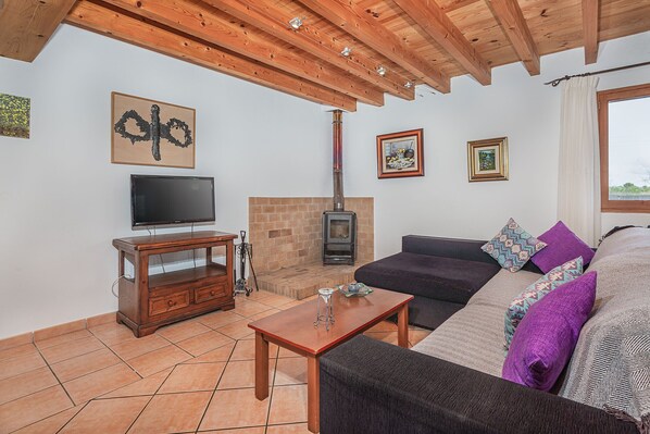 A living room with a fireplace, wooden ceiling beams, a sofa, and a television.