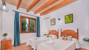 A room with two beds, a wooden cabinet, a window with blue curtains, and a wall-mounted air conditioner. - Villa Can Paxaco - By Dream Villas Pollensa (Alcudia)