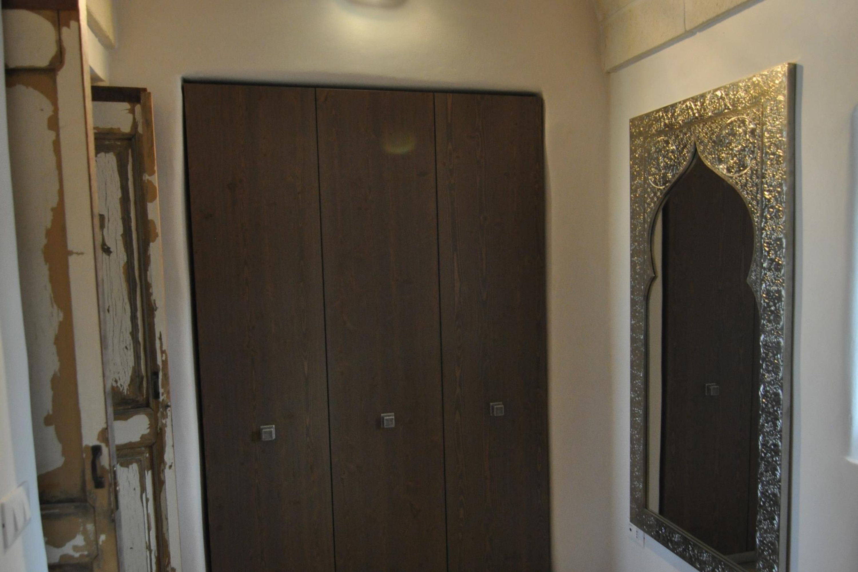 A room with a wooden wardrobe, a decorative mirror, and a partially visible door.