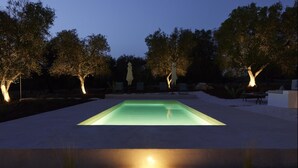A rectangular swimming pool with a lighted edge, surrounded by trees and outdoor seating. - Trullo dei Noci con Piscina Privata (Ceglie Messapica)